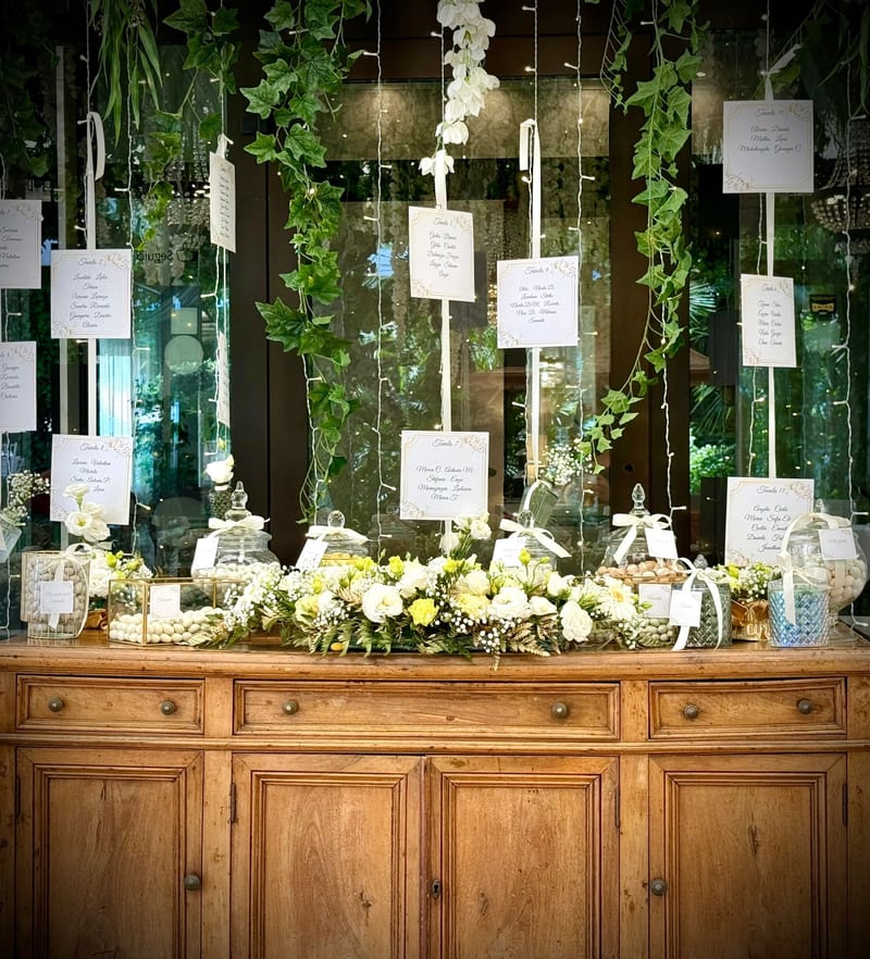 Tableau de mariage su credenza in legno con cartellini appesi tra le piante