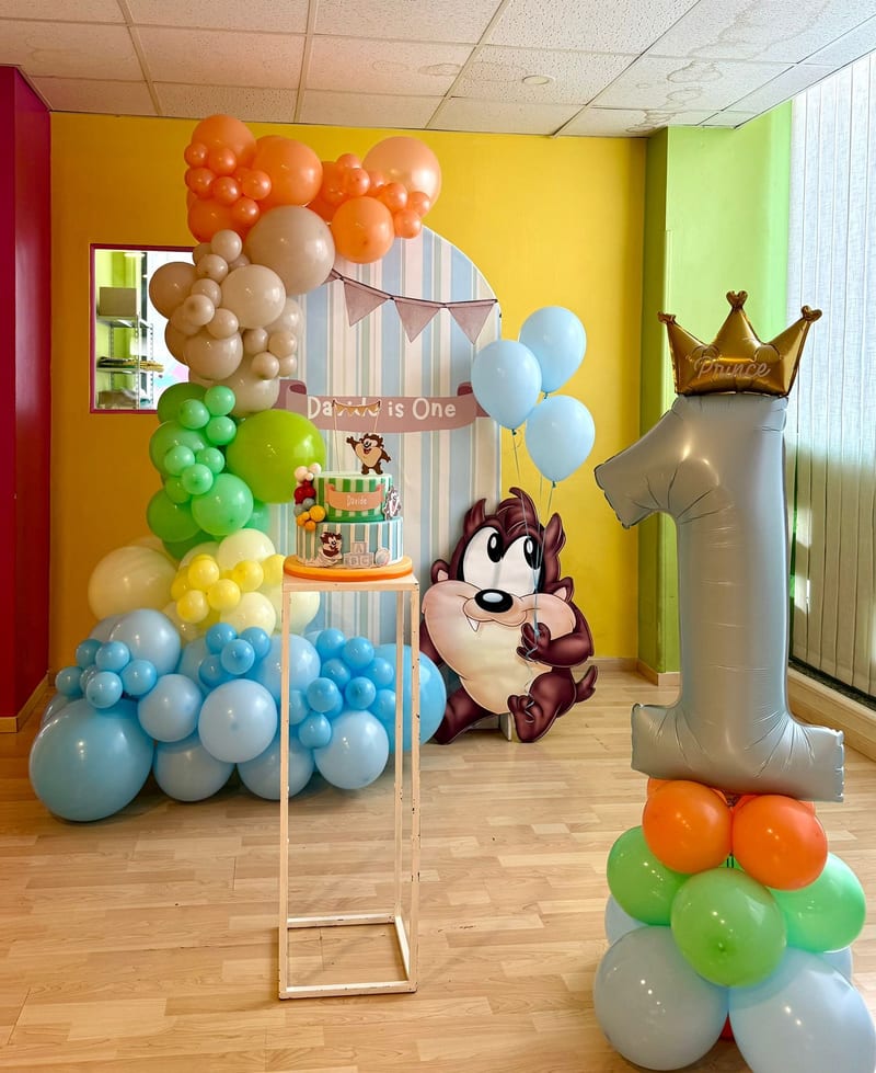 Allestimento compleanno a tema cartoni animati con arco di palloncini colorati e numero uno gigante