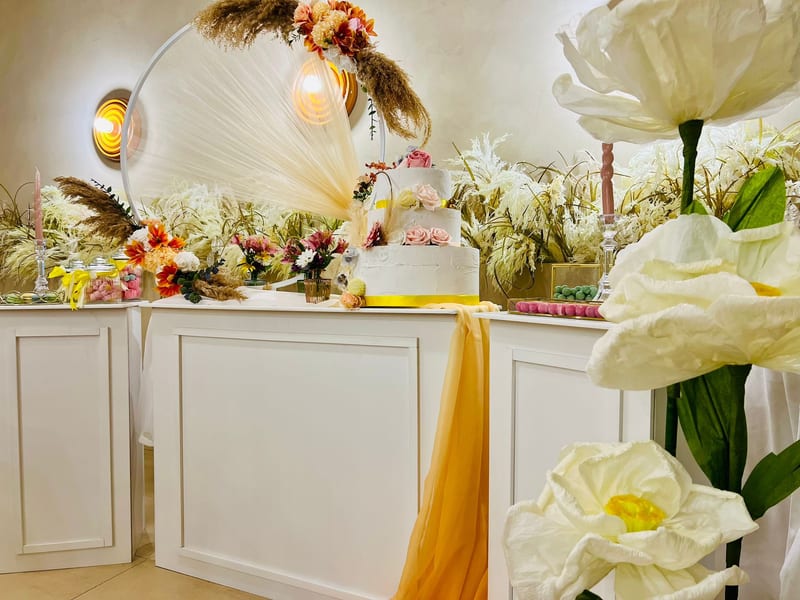 Tavolo dolci per comunione con grandi fiori di carta bianchi e drappeggio arancione