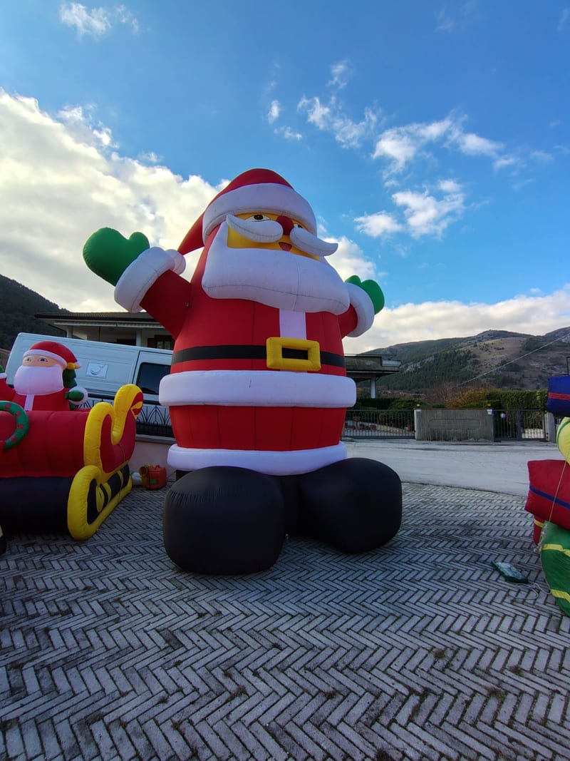 Babbo Natale gonfiabile gigante con slitta installato in piazza, montagne sullo sfondo
