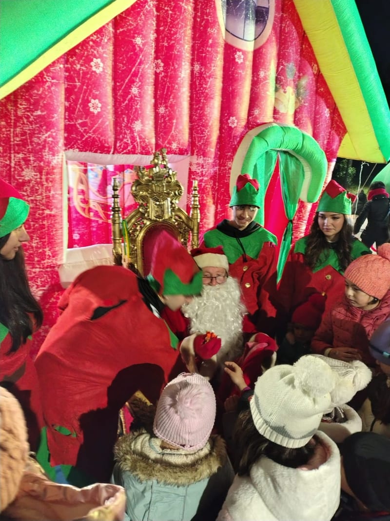 Babbo Natale seduto sul trono accoglie i bambini all'interno della casetta, affiancato dagli elfi